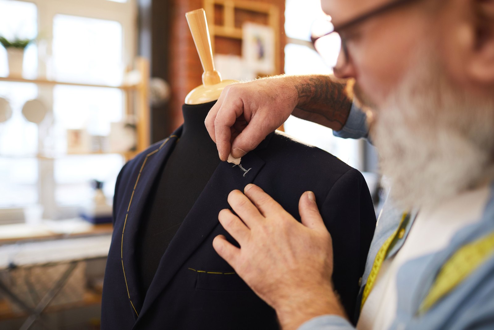 A tailor marking a navy suit jacket on a dress form